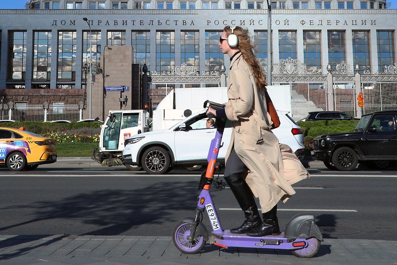 Девушка на электросамокате едет на фоне Дома правительства России