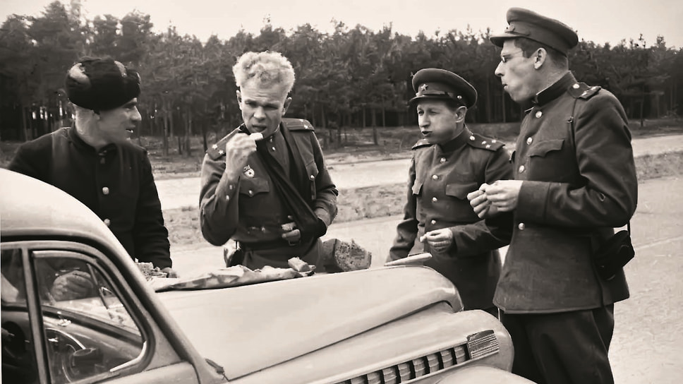 Кукрыниксы в Германии, 1945 год. Фотограф запечатлел остановку на автобане и перекус на капоте малолитражки Opel Olympia. На плече у Куприянова виден фотоаппарат — интересно, сохранились ли снимки из той поездки? Соколова в кадре нет, очевидно, он и снимает. Кто еще двое, неизвестно